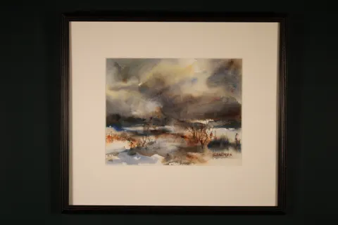 Framed watercolor winter landscape in blue-gray, brown, rust, and white tones. Snow-covered ground stretches beneath a dramatic cloudy sky, with sparse dark vegetation and distant landscape forms breaking through the wintry scene.