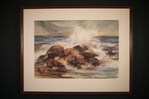 Large framed watercolor of a rocky coastal shoreline at Bar Harbor, Maine. Blue-gray ocean waves break against large reddish-brown and gray foreground rocks, with additional rocky outcrops extending into the water beneath a pale, misty sky. Signed “S. HOLMES” at lower left.